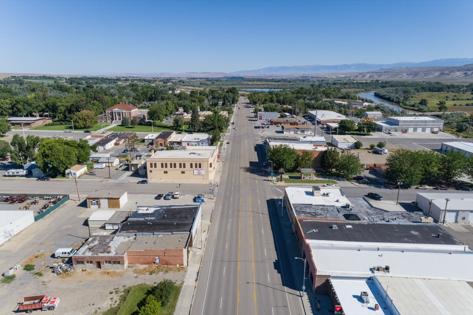 Aerial view down Basin's main street, Big Horn County, Wyoming — brick downtown storefronts with the Bighorn River and distant mountains beyond