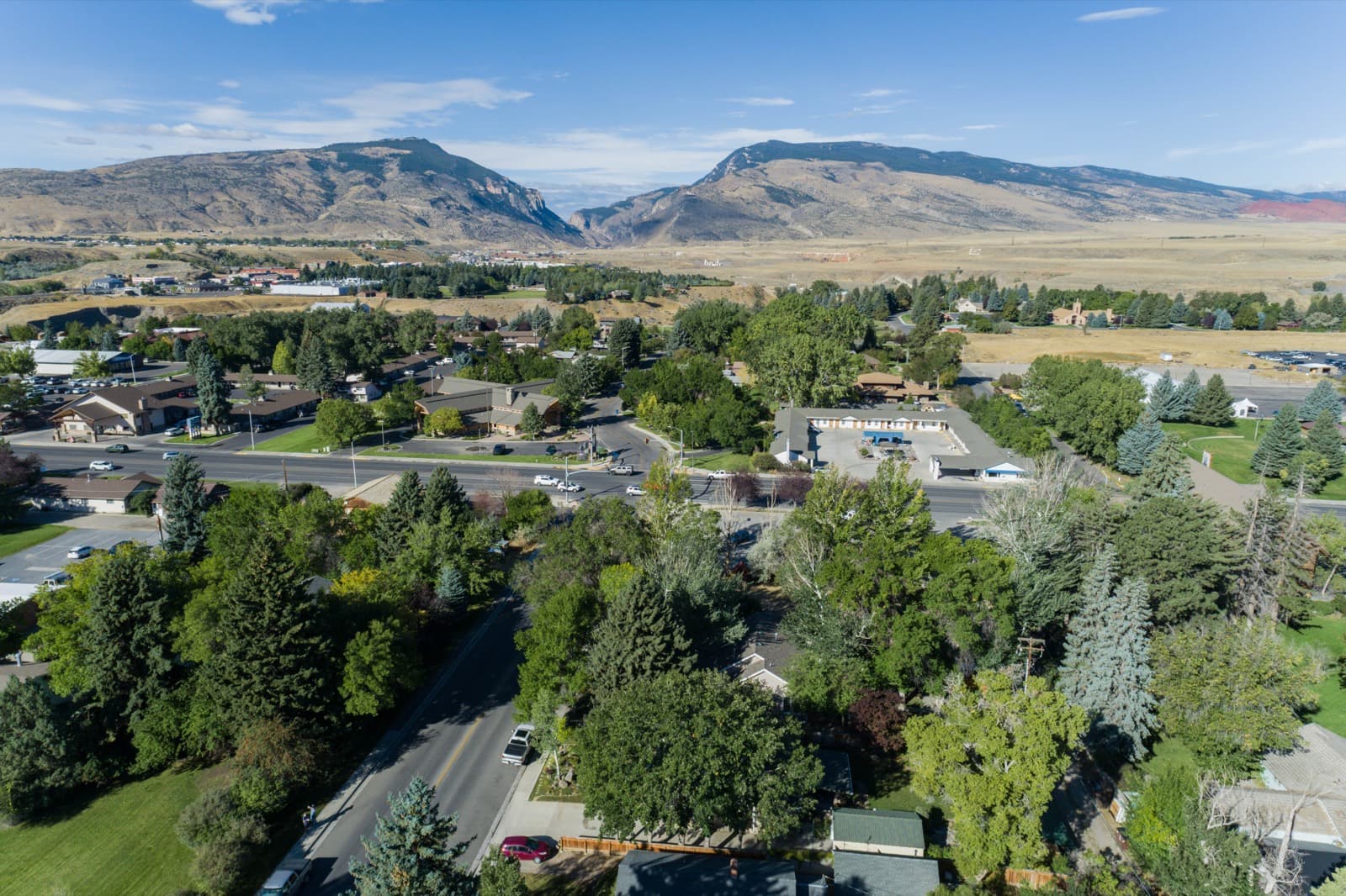 Aerial view of tree-lined residential Cody, Wyoming, with the Absaroka foothills and the mouth of the Shoshone River canyon rising west of town