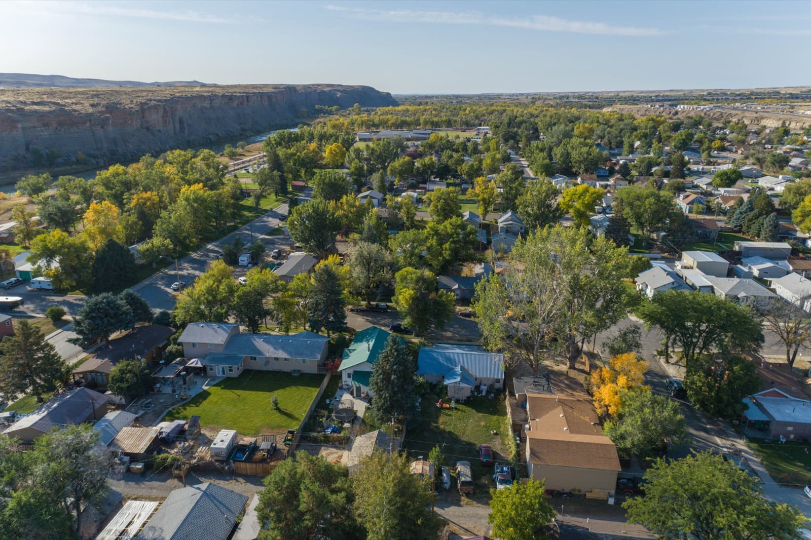 Aerial view of Greybull, Wyoming — residential streets and autumn cottonwoods along the Bighorn River, with sandstone bluffs on the horizon