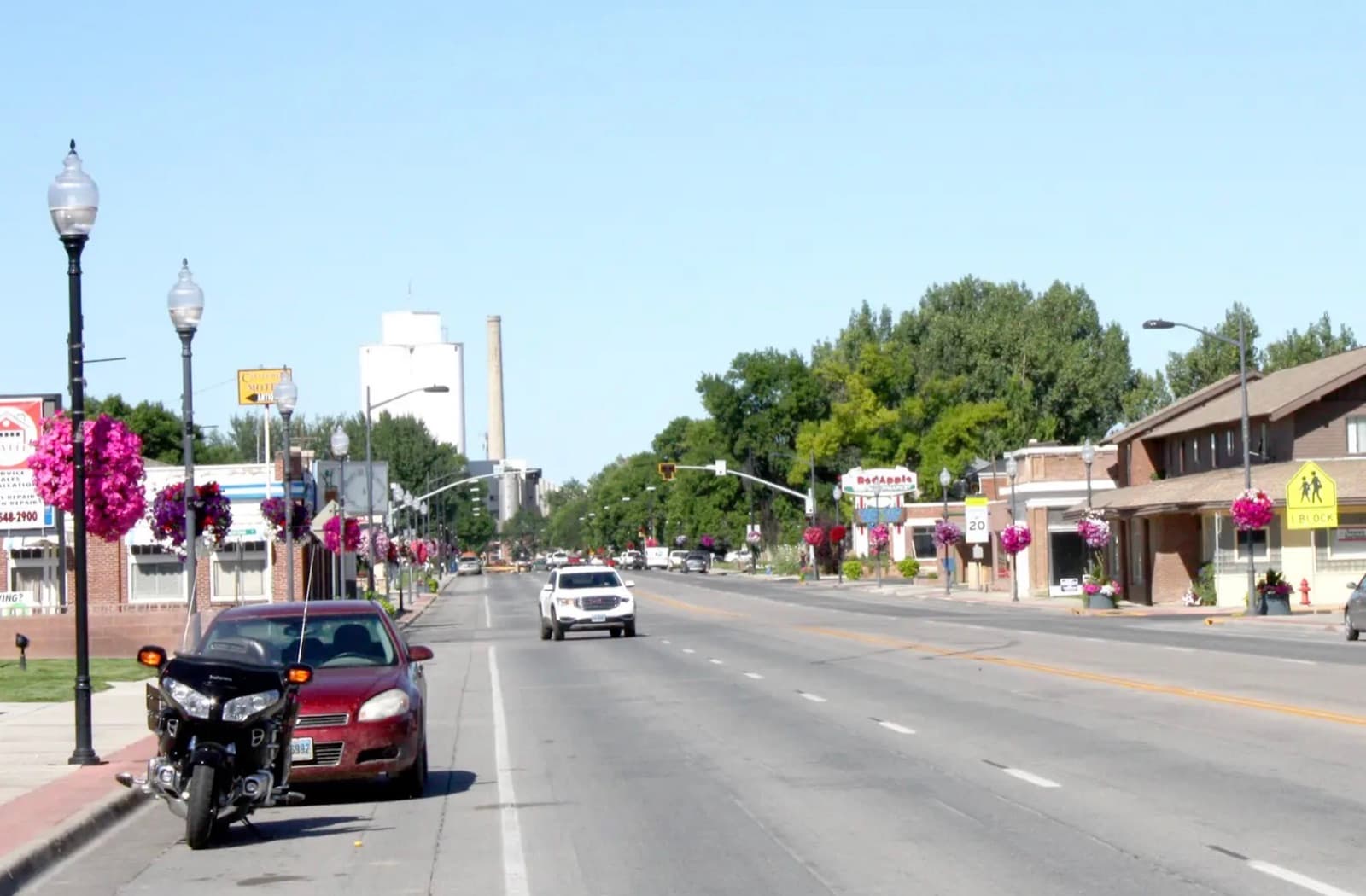 Main Street in Lovell, Wyoming — downtown storefronts lined with the town's signature rose baskets, with the Western Sugar plant rising in the distance