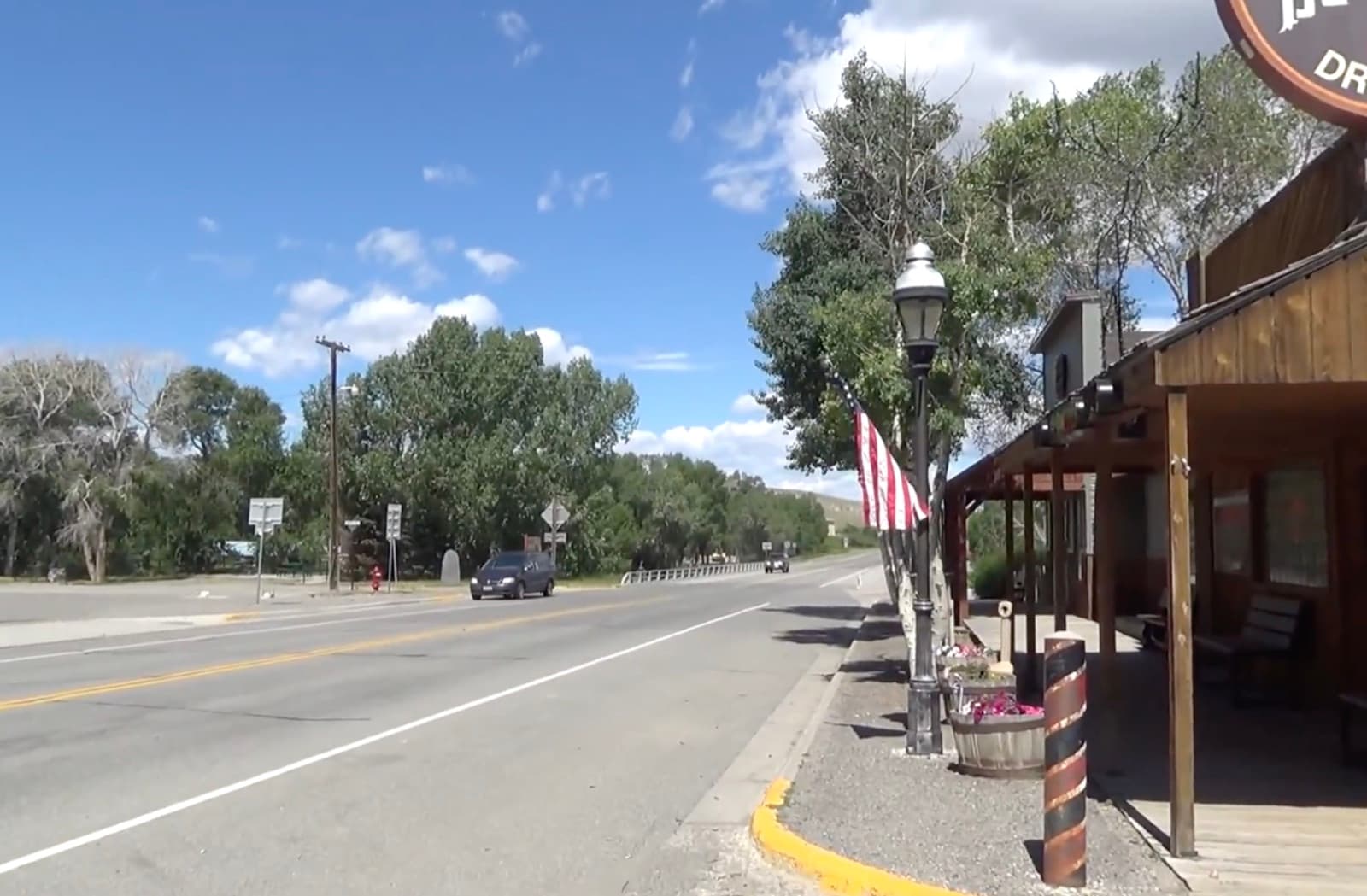 Main street in Meeteetse, Wyoming — the town's historic wooden boardwalk and storefronts along the highway, with cottonwoods and open ranch country beyond