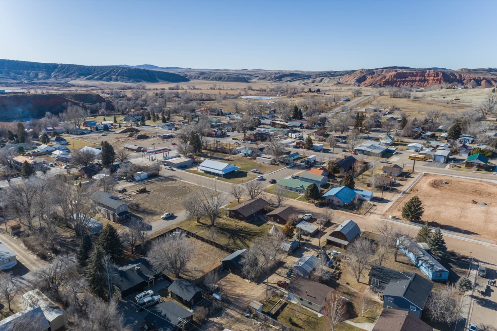 Aerial view of Ten Sleep, Wyoming, in late autumn — small-town streets framed by red-rock bluffs and badlands on the horizon