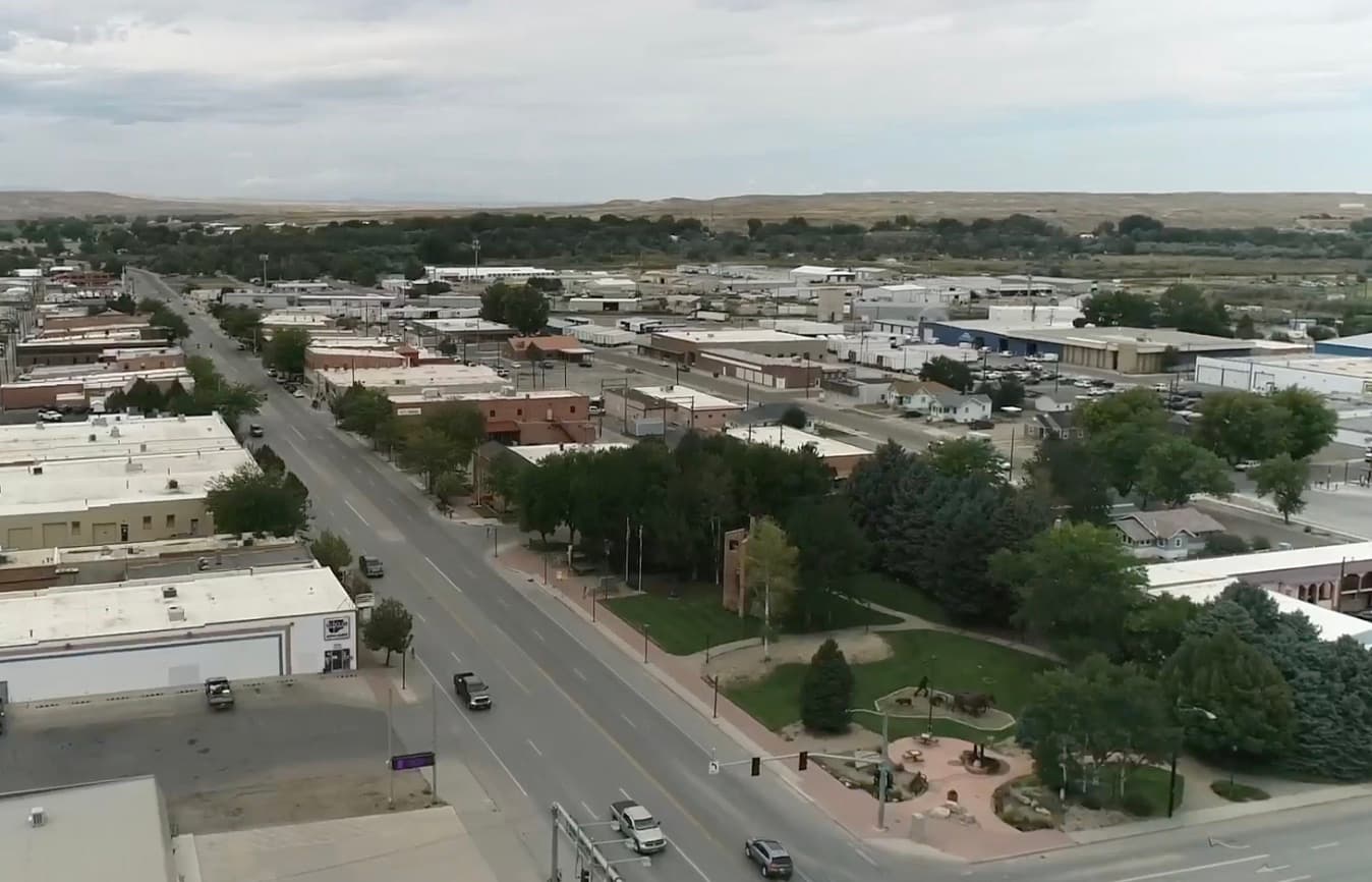 Aerial view of Worland, Wyoming — the downtown commercial corridor and tree-lined streets on the floor of the Bighorn Basin, with low bluffs on the horizon
